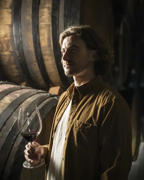 Matteo in cantina, fra le botti, con un calice di rosso in mano